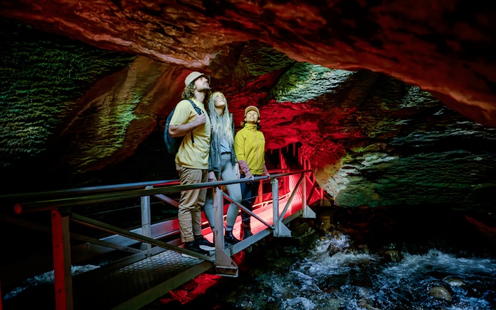 Tourists on a walkway exploring Te Anau Glowworm Caves with illuminated rock formations.