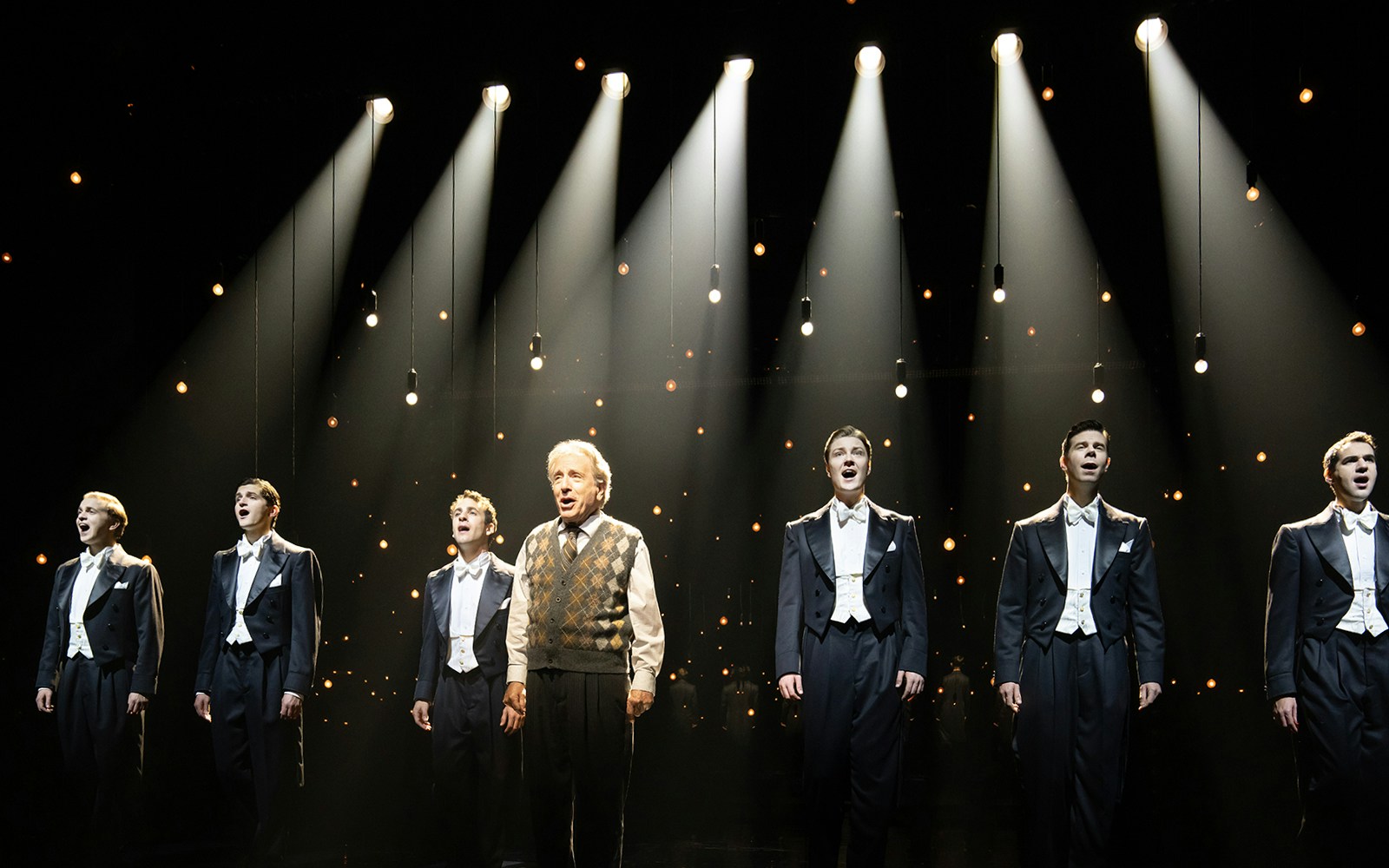 Performers singing on stage under spotlights in "Harmony: A New Musical".