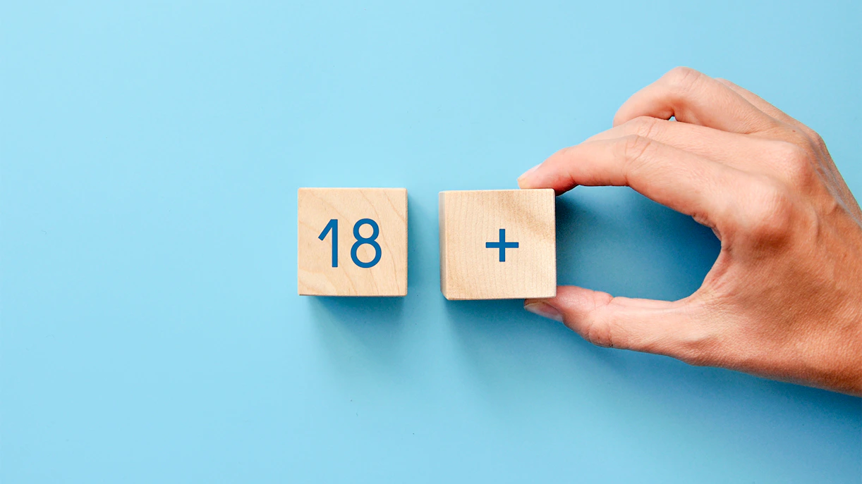Hand holding wooden blocks showing 18 plus, indicating age limit