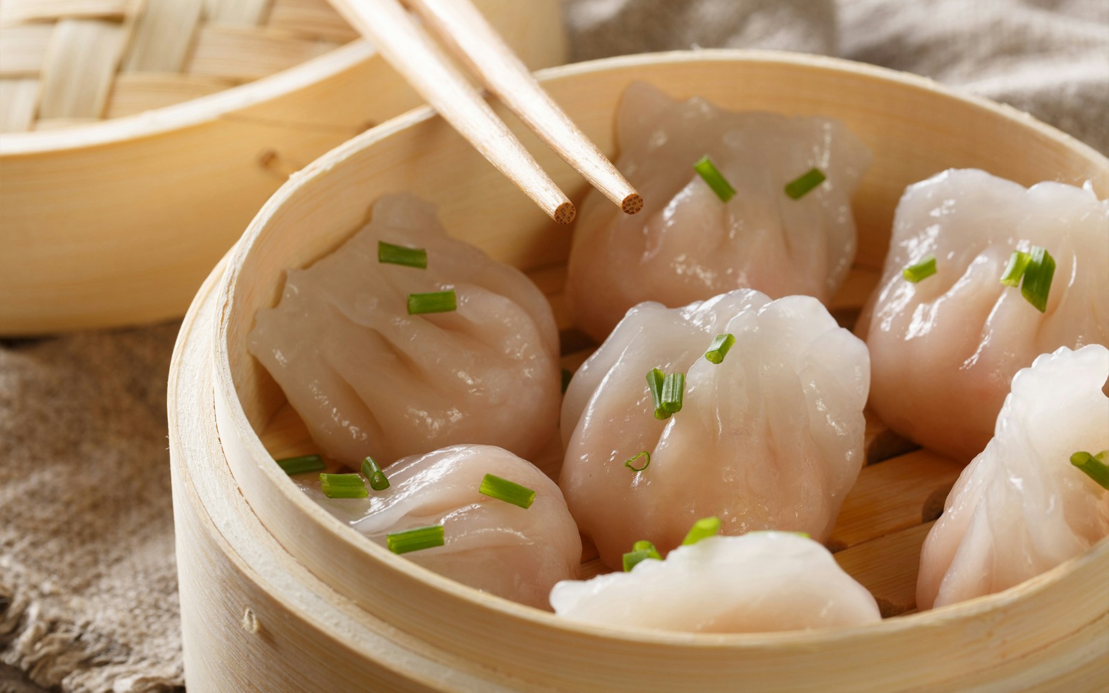 Steamed dumplings in a bamboo basket with chopsticks, dim sum experience.