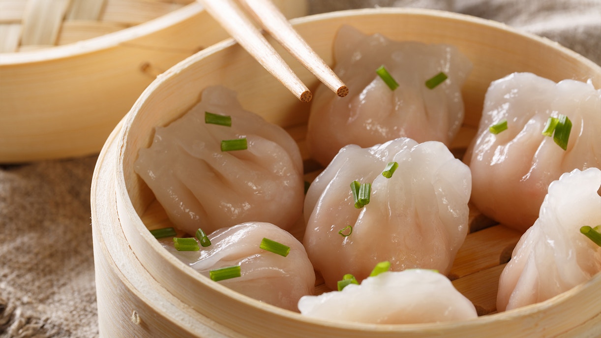 Steamed dumplings in a bamboo basket with chopsticks, dim sum experience.