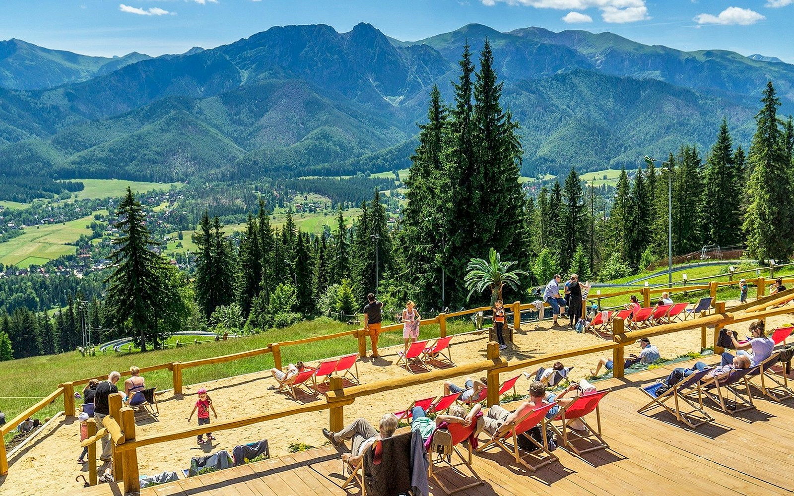 High Tatras view from a sunbathing area with people relaxing in deck chairs.