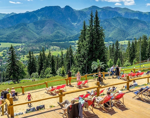 High Tatras view from a sunbathing area with people relaxing in deck chairs.
