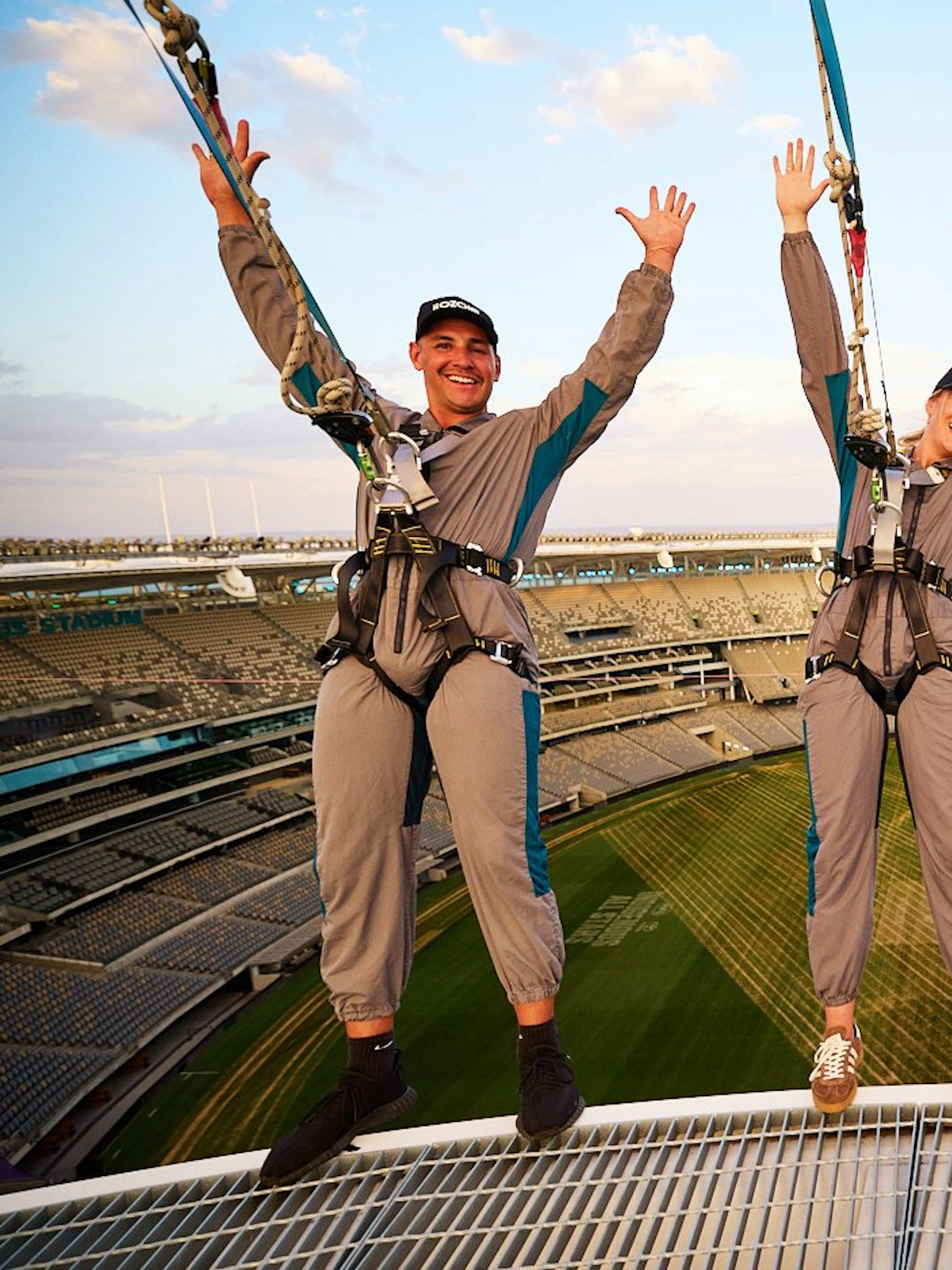 Visitors harnessed on stadium roof edge during Vertigo by Twilight experience.
