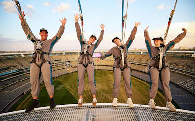 Visitors harnessed on stadium roof edge during Vertigo by Twilight experience.