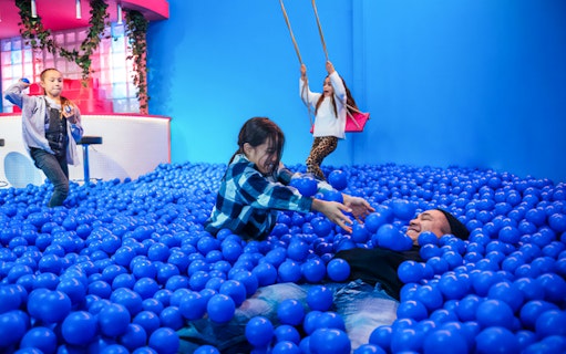 Children playing in a blue ball pit at Youseum, an interactive museum experience.