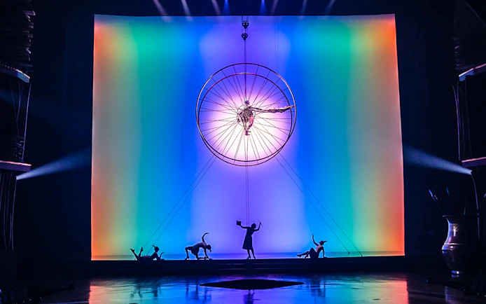 Acrobats performing under a large wheel with colorful lights in "Drawn to Life" show.