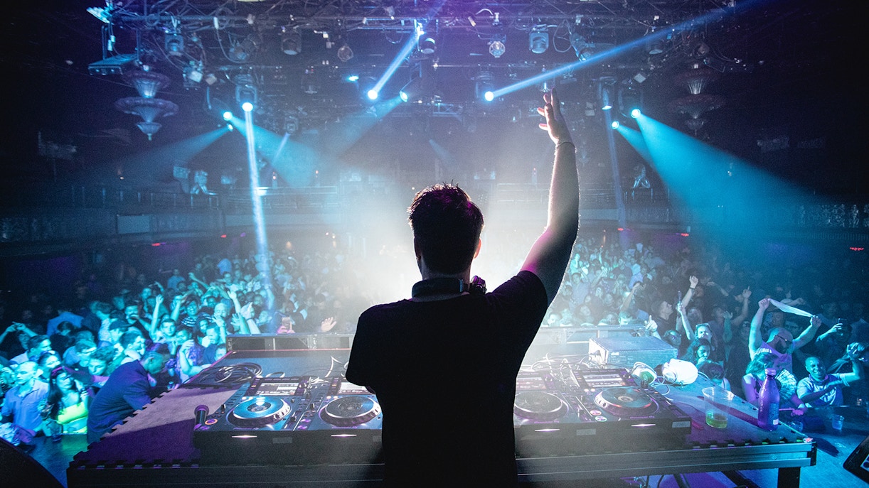 DJ performing at a nightclub with a crowd dancing under blue lights.