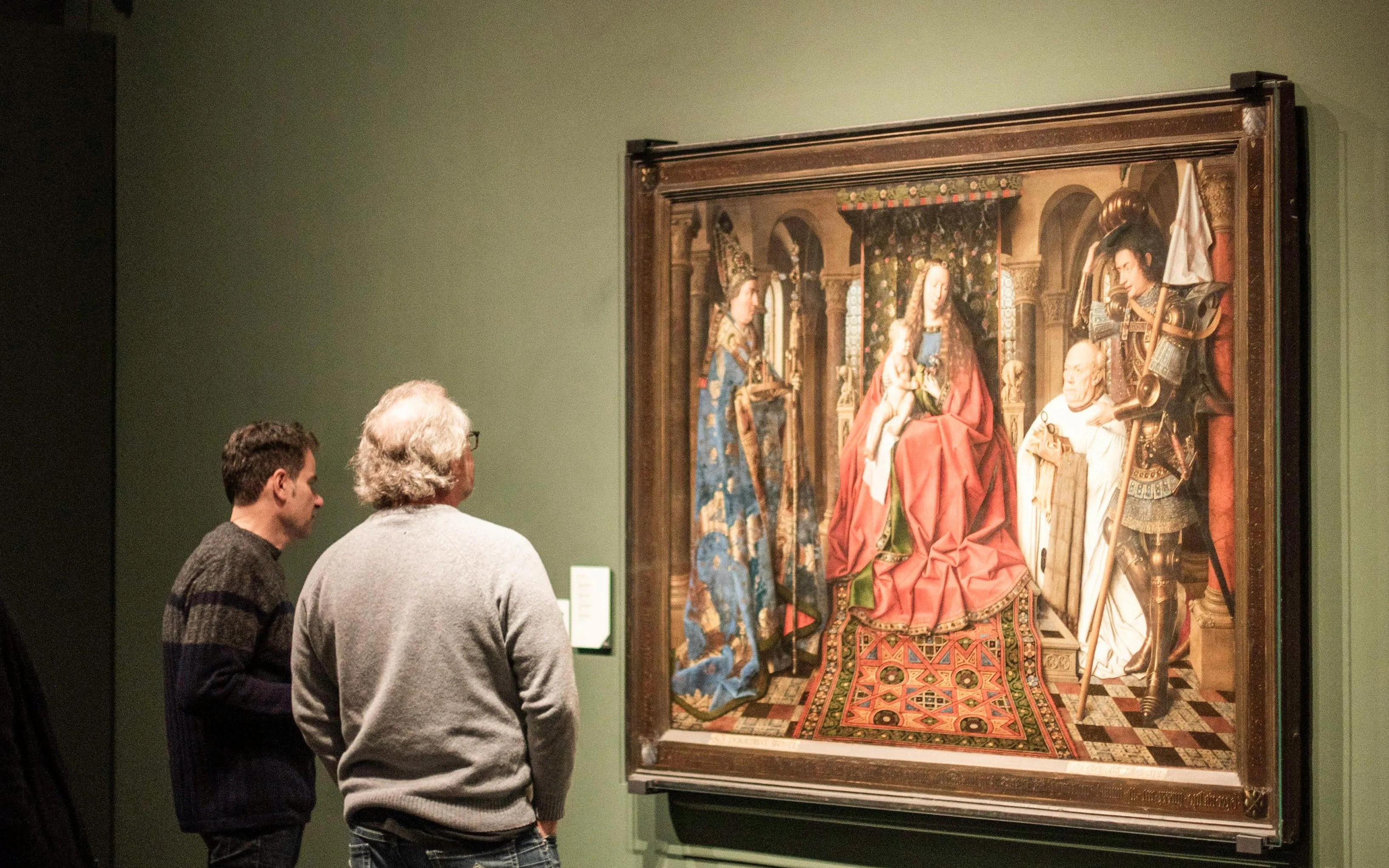 Visitors viewing a historical painting at Groeningemuseum, Bruges.