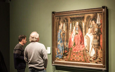 Visitors viewing a historical painting at Groeningemuseum, Bruges.