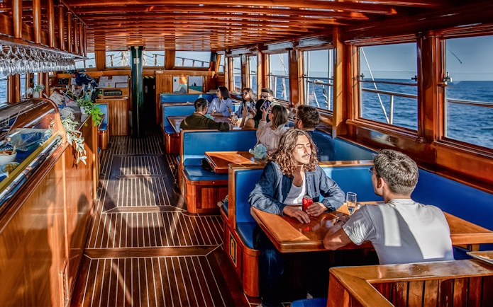 People enjoying a meal inside a catamaran with ocean views in Barcelona.
