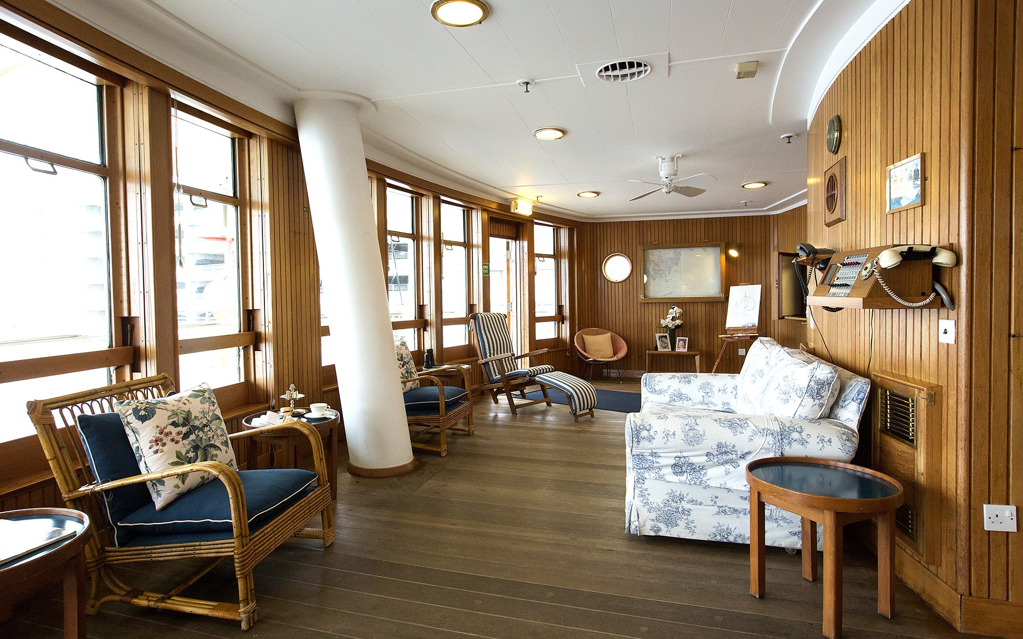 Wood-paneled sun lounge with wicker chairs and floral cushions on a cruise ship.