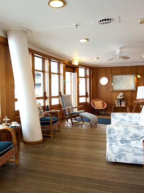 Wood-paneled sun lounge with wicker chairs and floral cushions on a cruise ship.