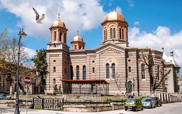 Orthodox Cathedral of Saints Peter and Paul in Constanta with copper domes and a seagull flying above.