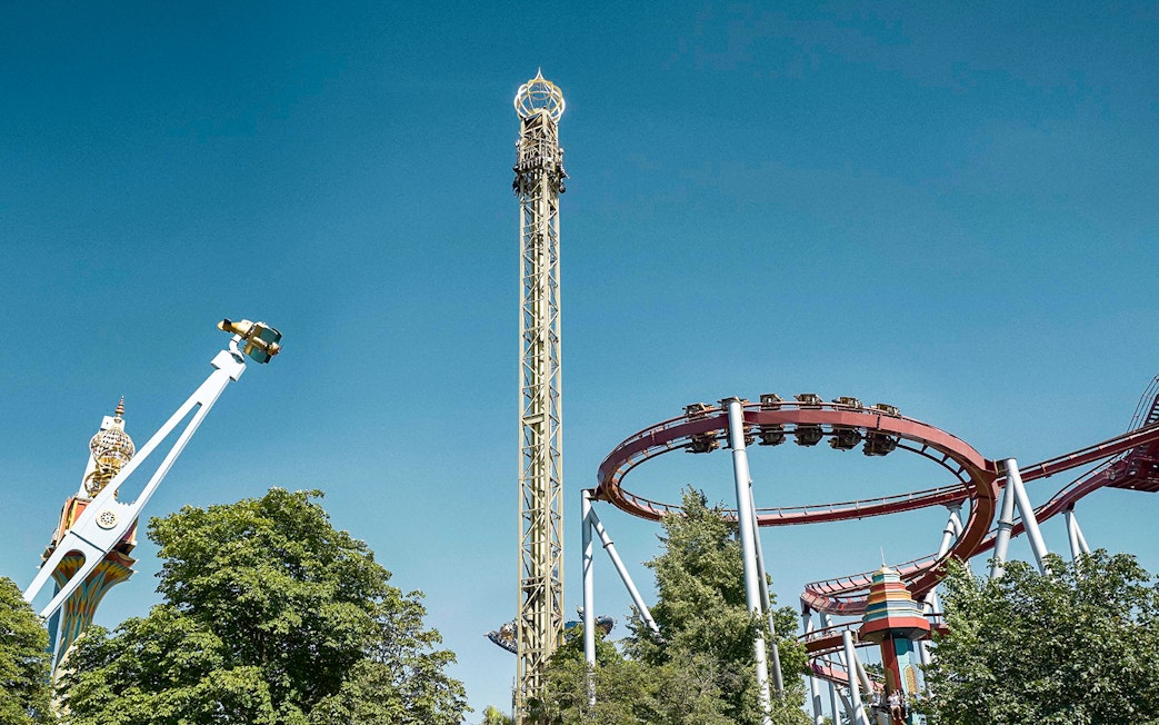 Roller coasters and rides at Tivoli Gardens, Copenhagen, under a clear blue sky.