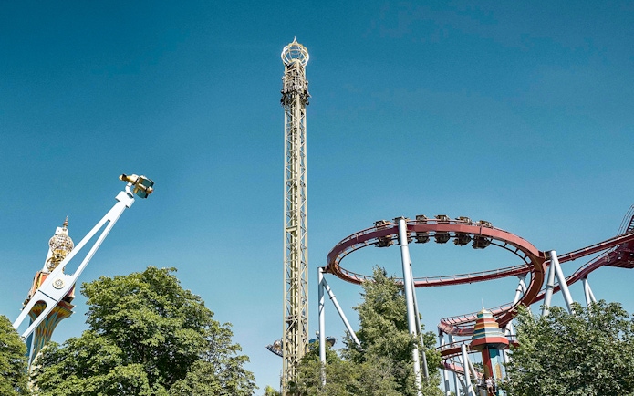 Roller coasters and rides at Tivoli Gardens, Copenhagen, under a clear blue sky.
