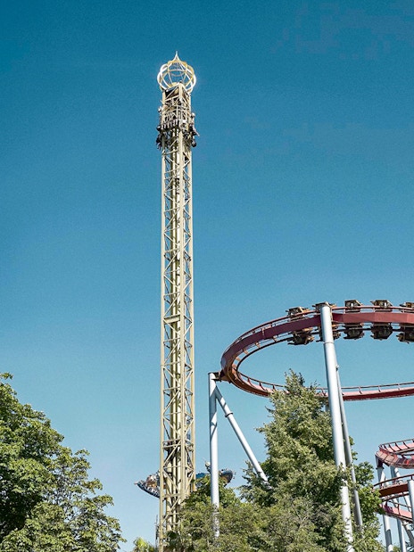 Roller coasters and rides at Tivoli Gardens, Copenhagen, under a clear blue sky.