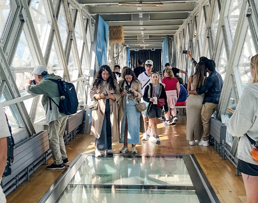Visitors walking on the glass walkway inside Tower Bridge, London.