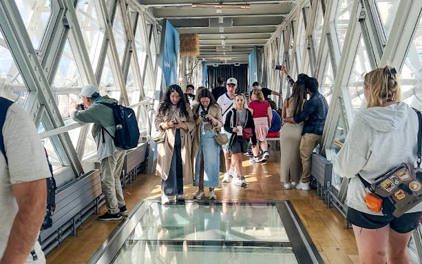 Visitors walking on the glass walkway inside Tower Bridge, London.