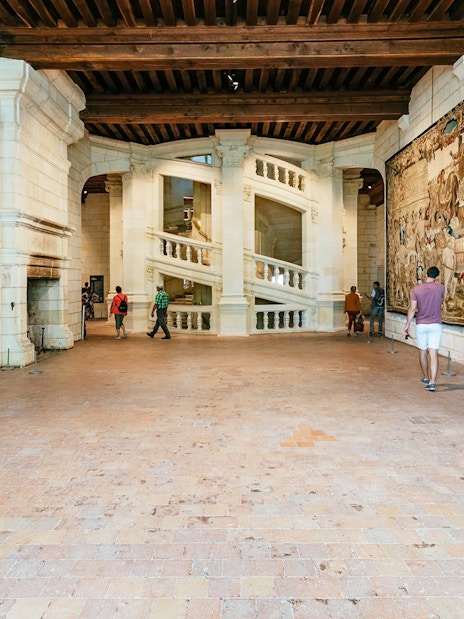Visitors near the helix staircase in Chambord Castle, France, with tapestries on the walls.