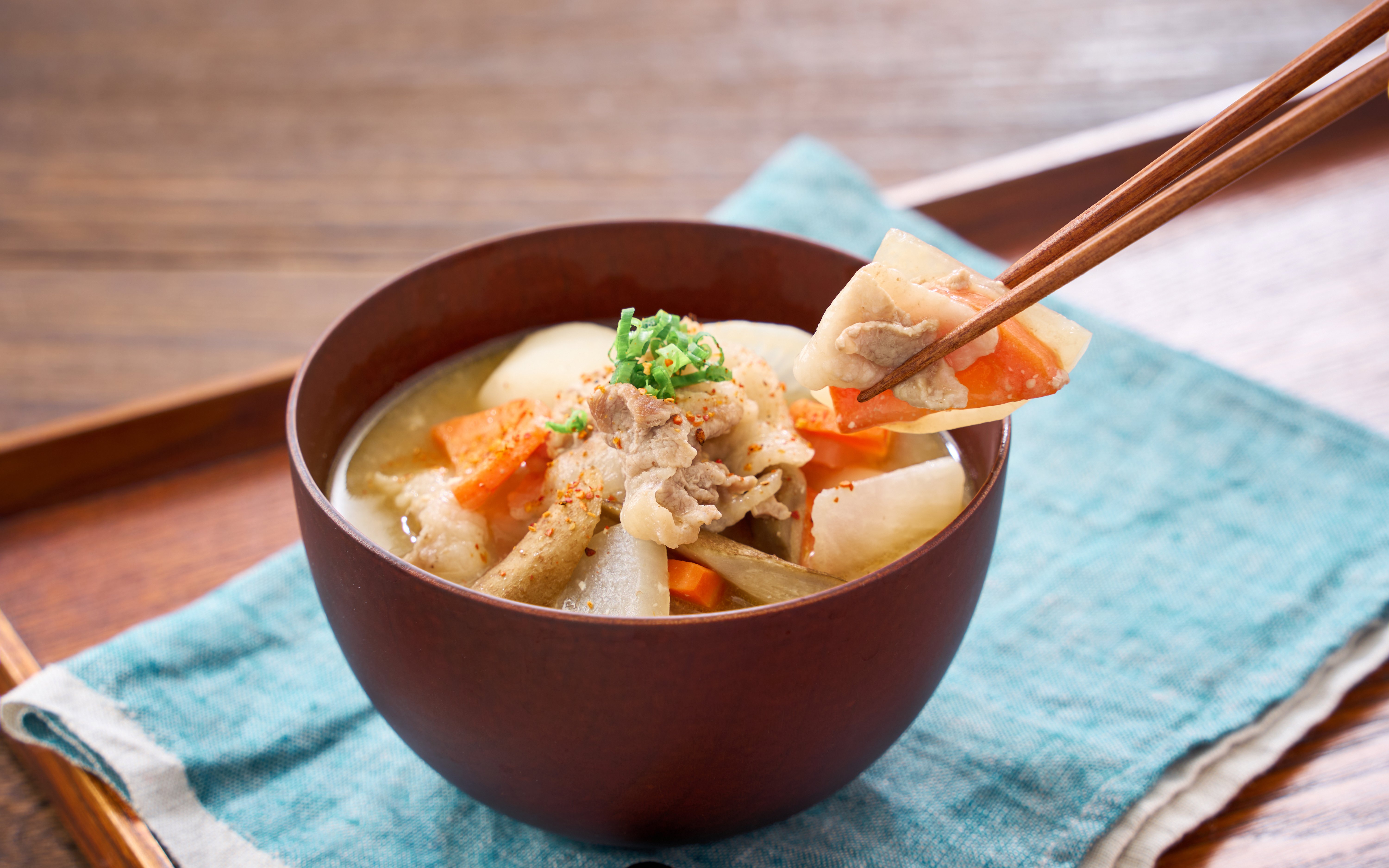 Pork miso soup with root vegetables in a wooden bowl, garnished with green onions.