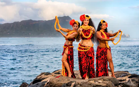 Hula dancers performing at Na Lei Aloha Luau, Waikīkī with ocean and mountain backdrop.