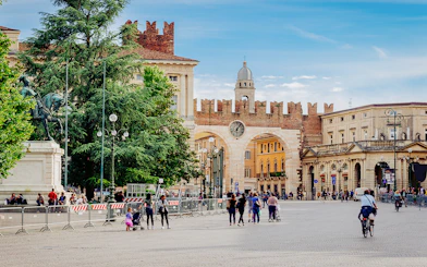 Medieval gates and clock tower on Piazza Bra, Verona, Italy, with people walking nearby.