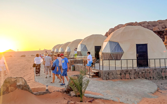 Tourists walking past dome tents at sunset in Wadi Rum desert, Jordan.