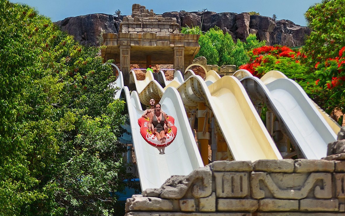Visitors on a water slide at Aqualand Maspalomas, surrounded by lush greenery.