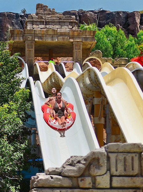 Visitors on a water slide at Aqualand Maspalomas, surrounded by lush greenery.