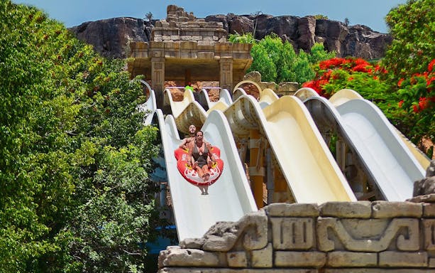 Visitors on a water slide at Aqualand Maspalomas, surrounded by lush greenery.