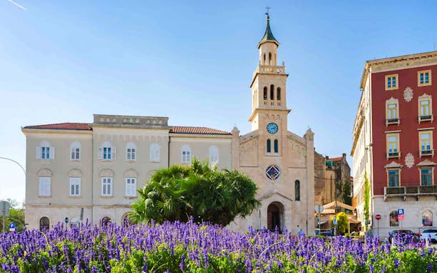 Historic church and colorful buildings in Split, Croatia, viewed from a garden on a panoramic bus tour.