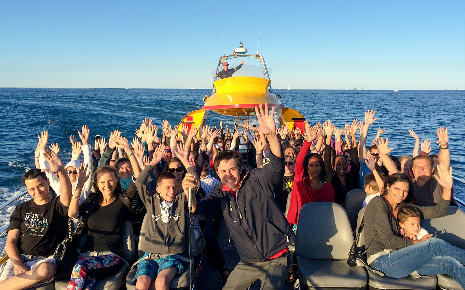 Tourists enjoying the Sea Dog Cruise on Lake Michigan with hands raised.