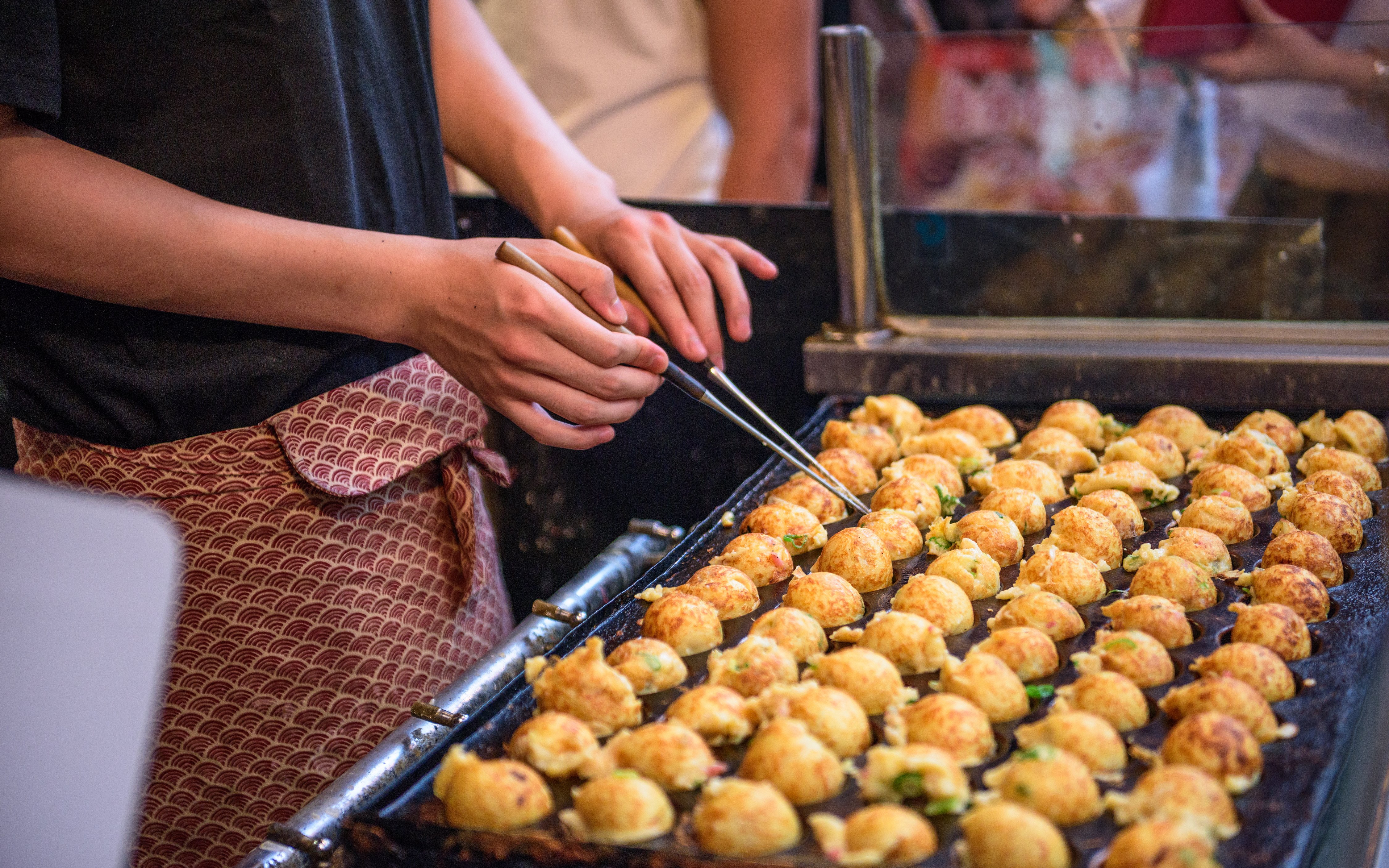 Vendor cooking takoyaki octopus balls on a grill in Osaka, Japan.
