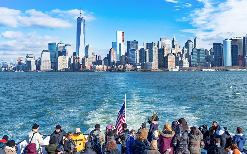 Tourists on a ferry with New York City skyline in the background.