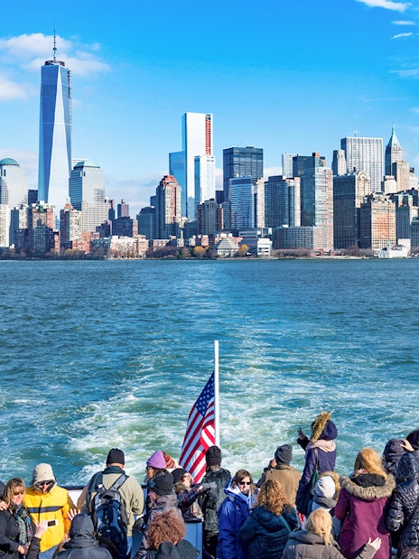 Tourists on a ferry with New York City skyline in the background.