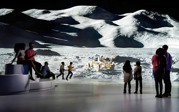 Group observing moon surface projection with lunar rover display.