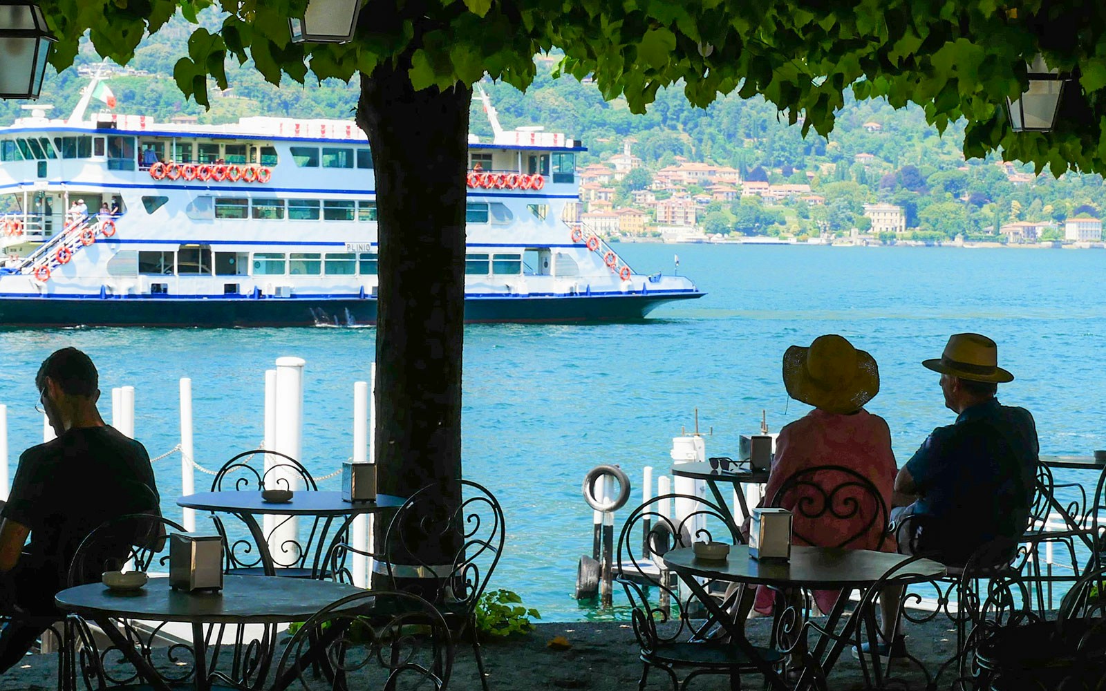 Tourists seated at a lakeside café watching a ferry on Lake Como during Bellagio and Varenna tour.