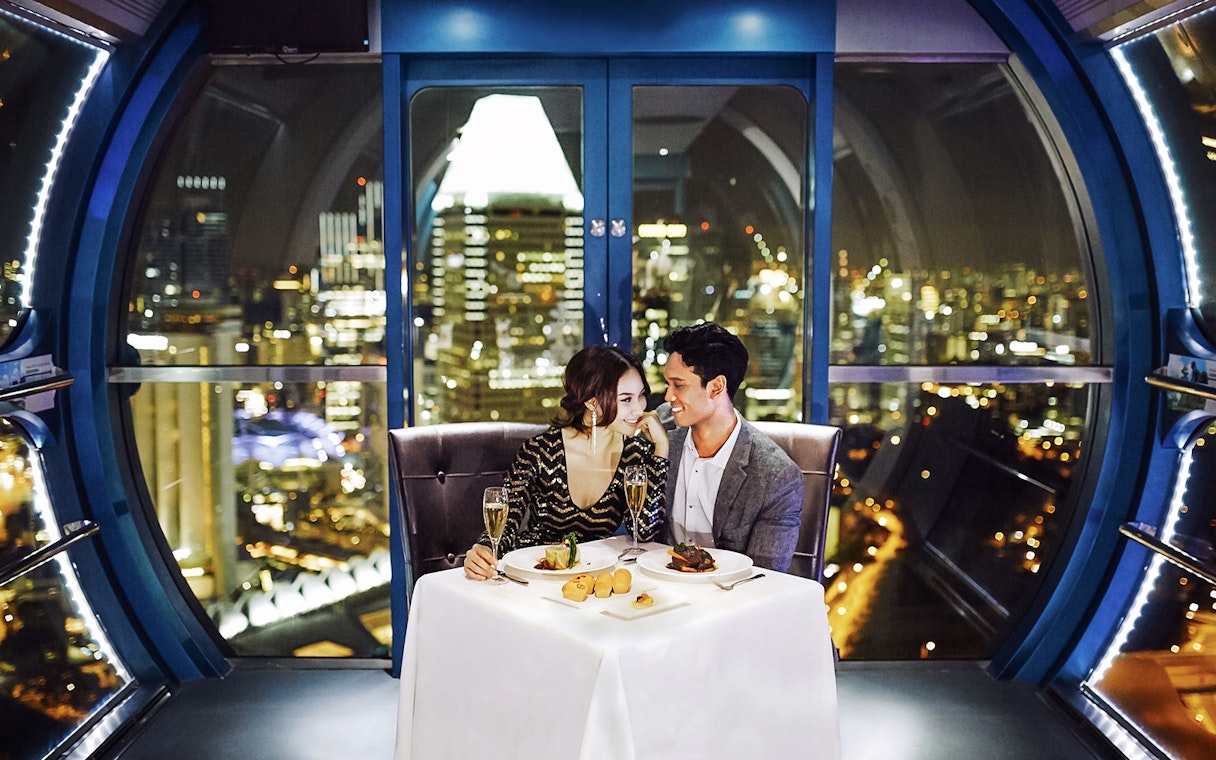 Couple dining in a Singapore Flyer capsule with city skyline view.