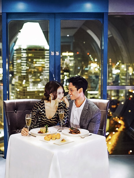 Couple dining in a Singapore Flyer capsule with city skyline view.