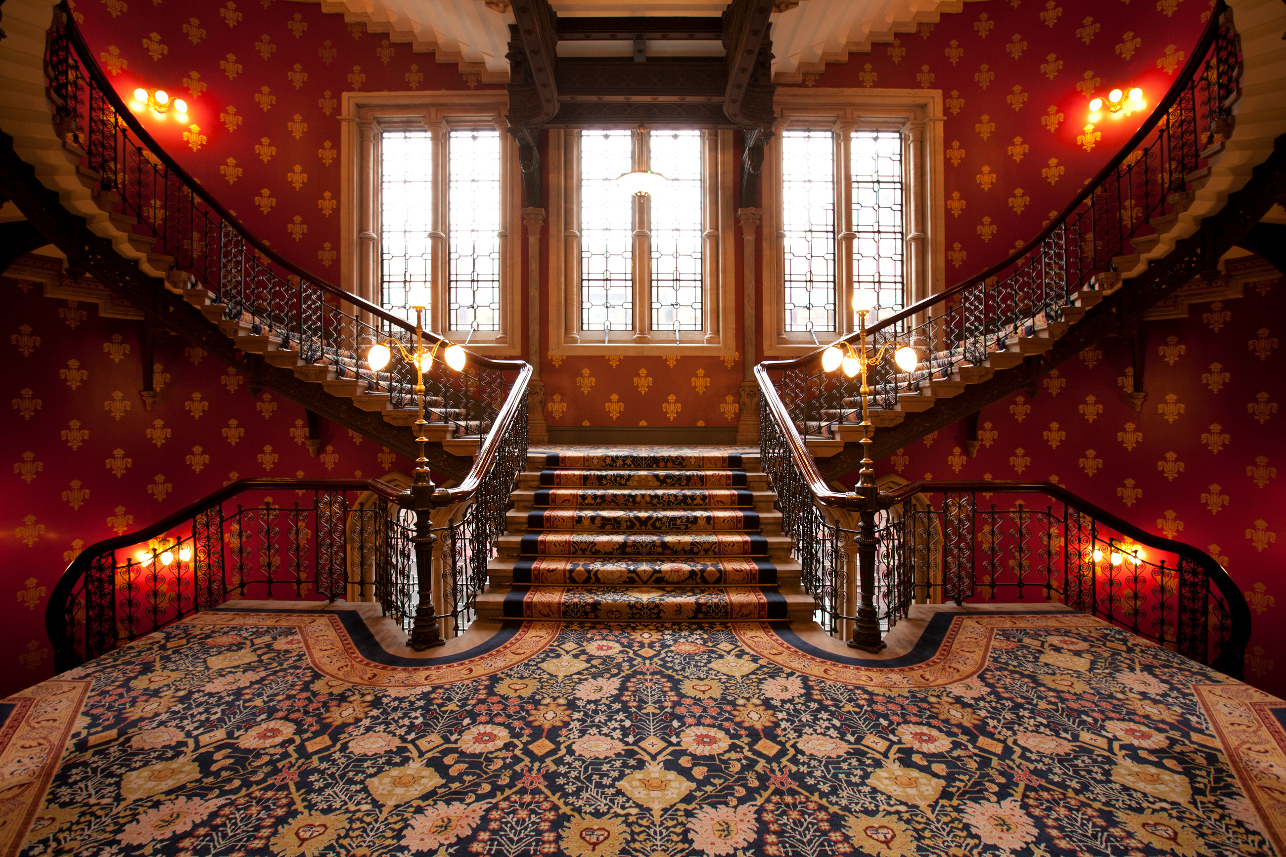 Grand staircase with ornate carpet and wrought iron railings in a castle interior.