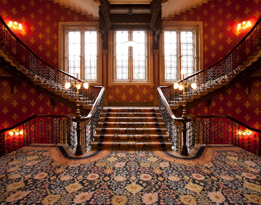 Grand staircase with ornate carpet and wrought iron railings in a castle interior.