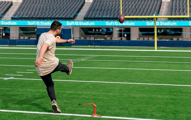 Person kicking football on SoFi Stadium field during tour.