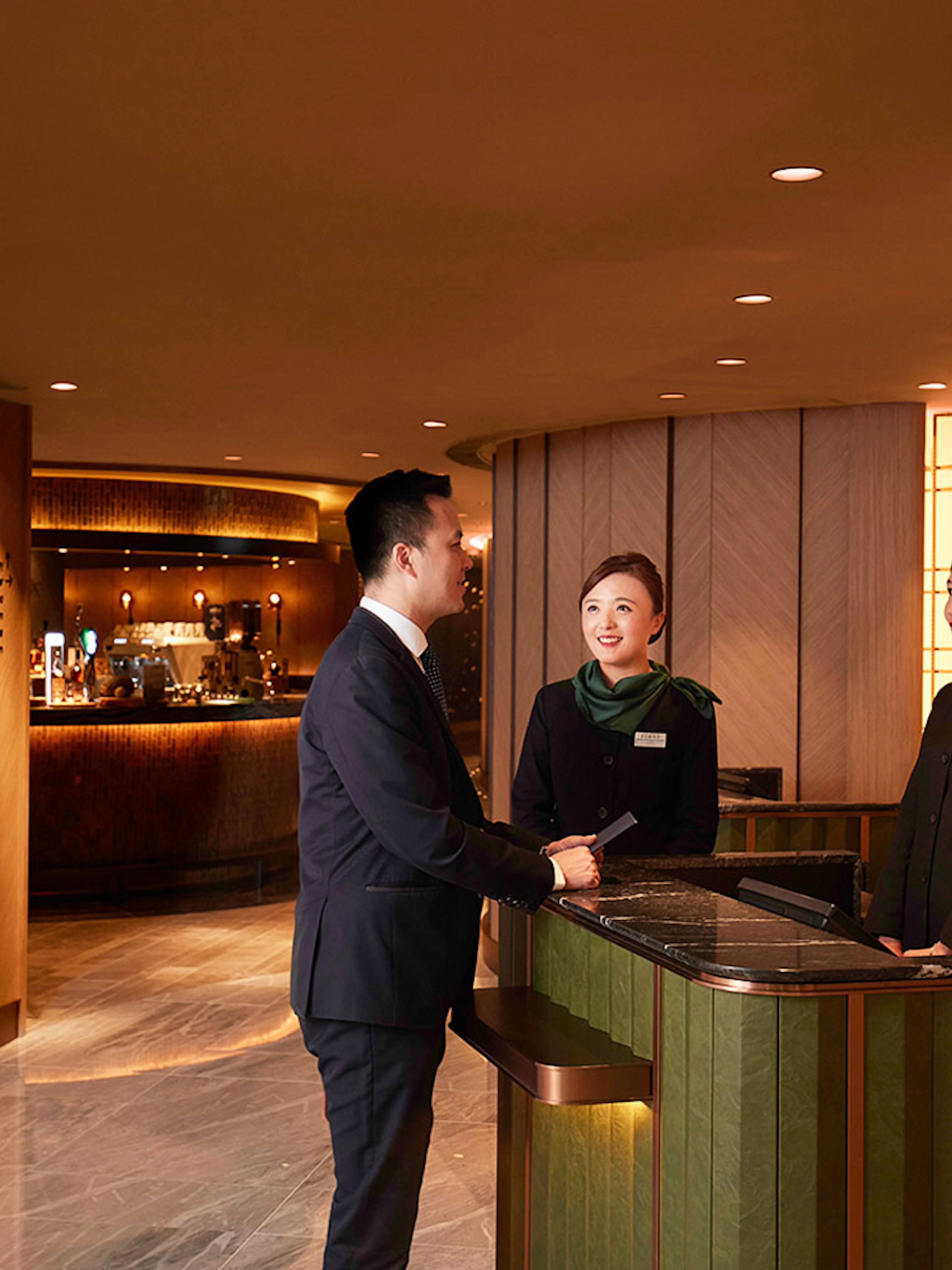 First-class lounge reception at Hong Kong International Airport with staff assisting a guest.