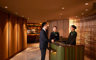 First-class lounge reception at Hong Kong International Airport with staff assisting a guest.