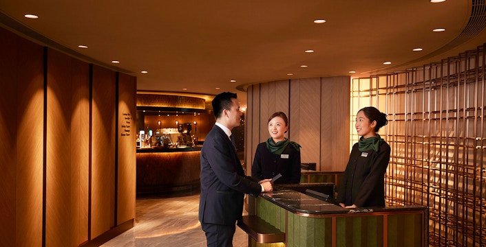 First-class lounge reception at Hong Kong International Airport with staff assisting a guest.