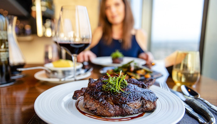 Gourmet ribeye steak with red wine on a dining table.
