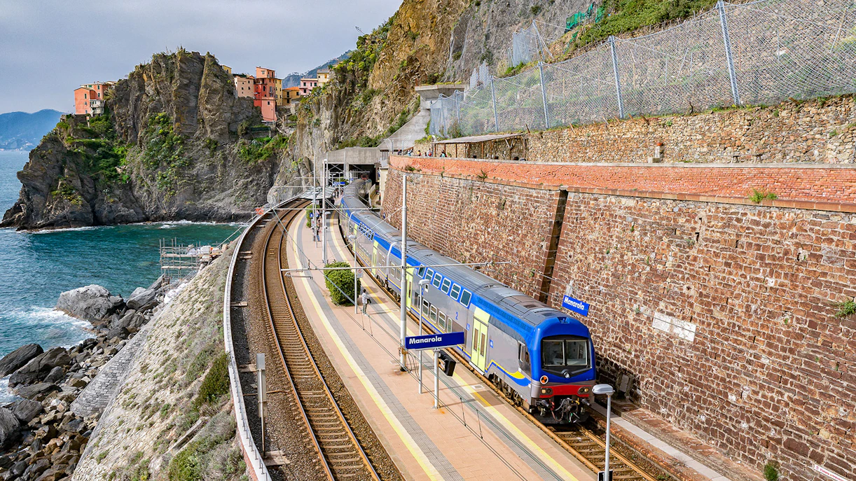 Train at Manarola station in Cinque Terre, Italy, with coastal cliffs and sea view.