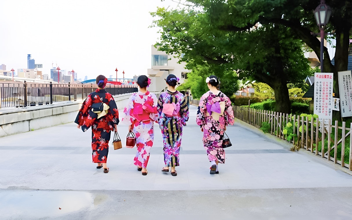 Women in colorful kimonos walking in Asakusa, Tokyo, near a riverside path.