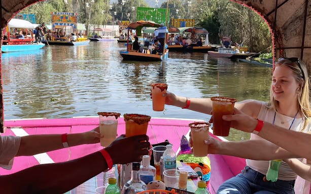 Guests toasting with drinks on a colorful boat in Xochimilco canals, Mexico City.